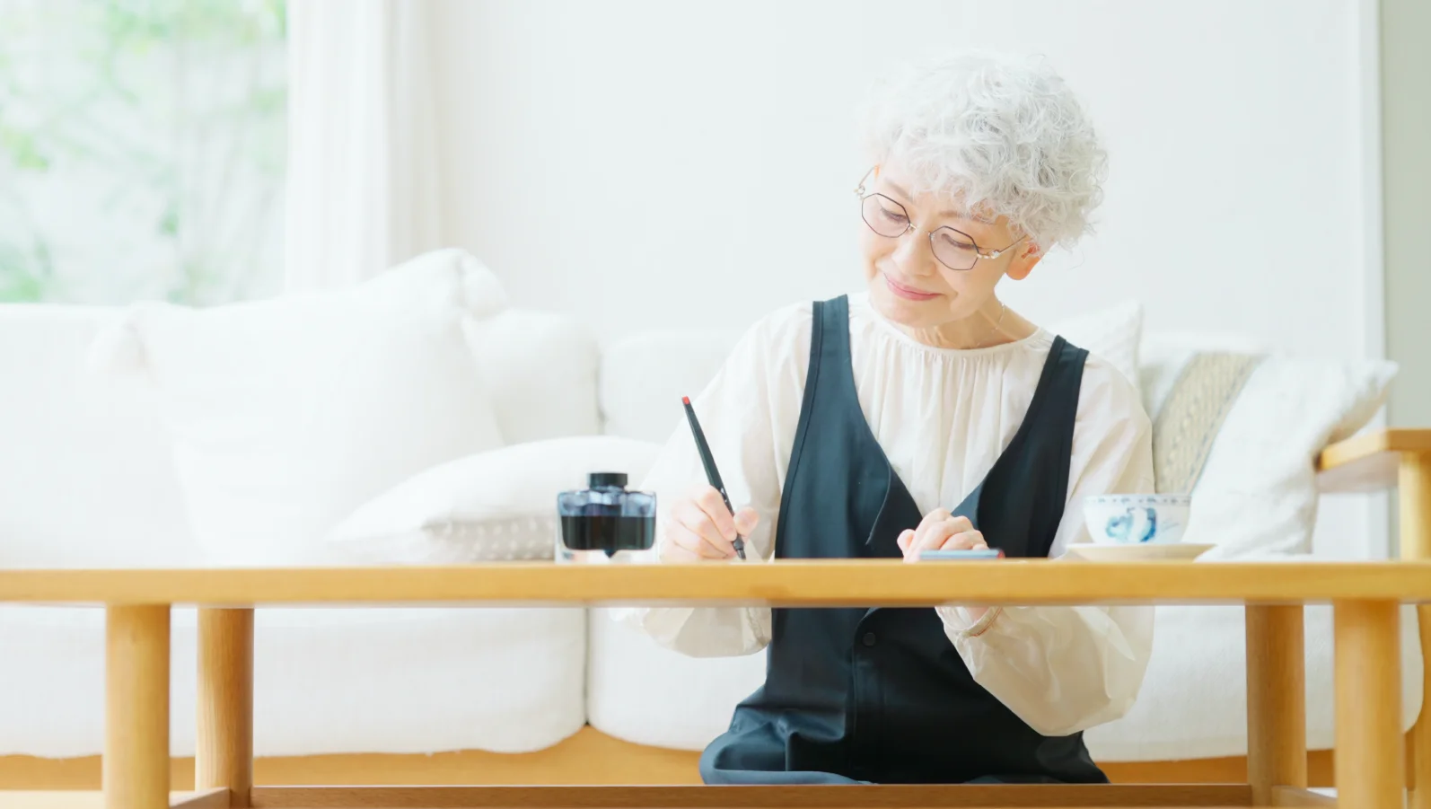 ソファでノートに書き込む高齢の女性