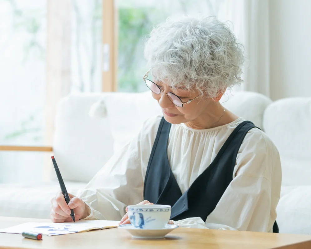 ノートに書き込みながらお茶を飲む高齢の女性