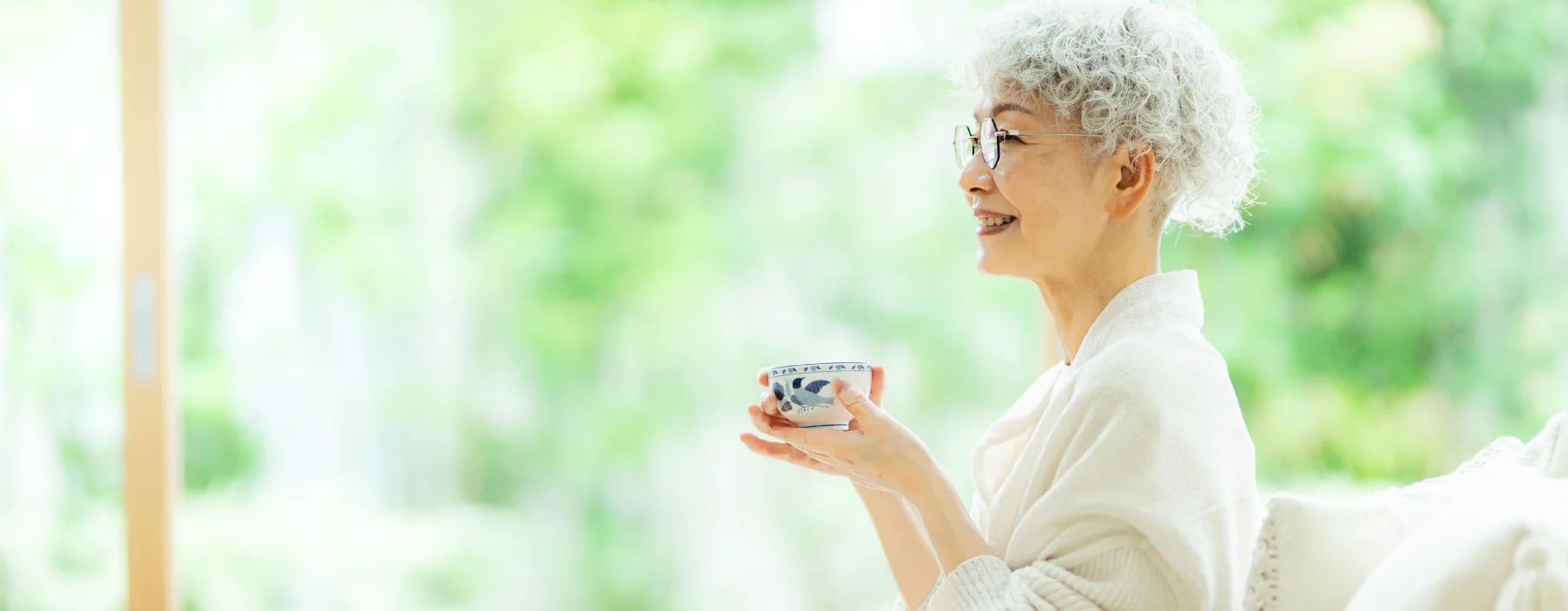 窓辺でお茶を楽しむ高齢の女性