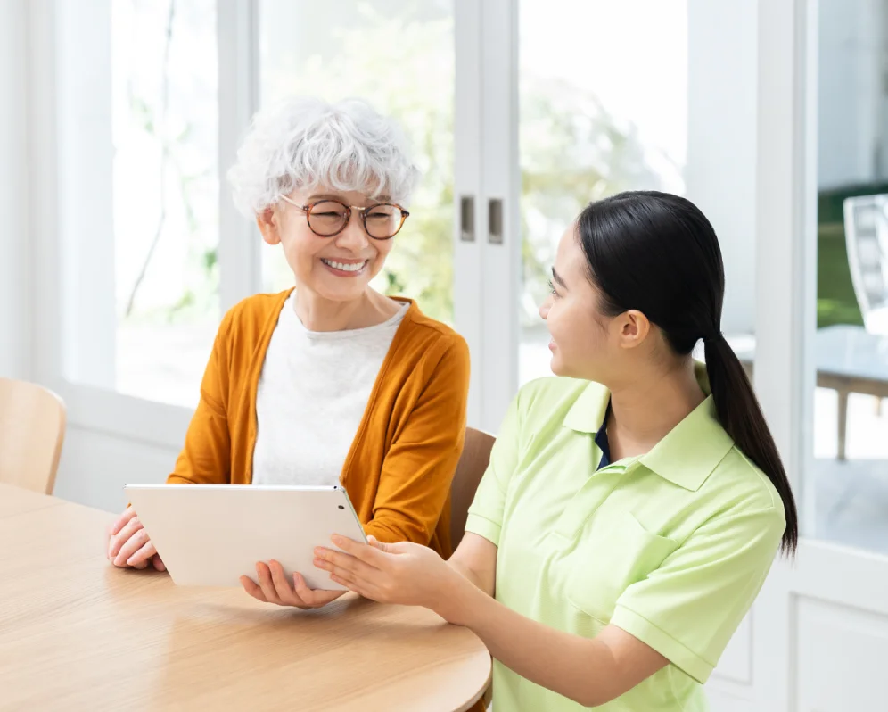 タブレットを前に笑顔で話す高齢の女性と介護スタッフ