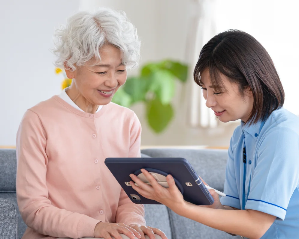 タブレットを見ながら説明を受ける高齢の女性と介護スタッフ