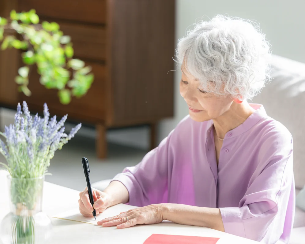 机に向かって書類に記入する高齢の女性